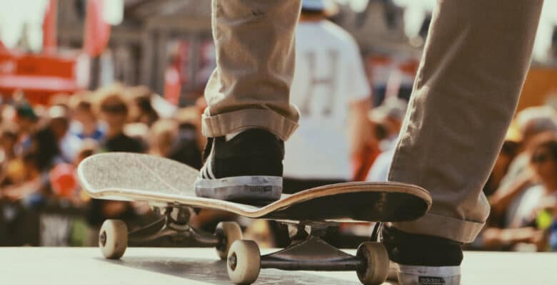 vue sur les pieds d'un homme portant un chino beige et des baskets foncées un pied posé sur un skate